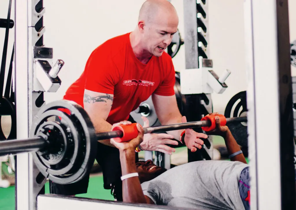 Chris Dellasega provides strength and conditioning coaching to a college basketball player from the University of Kansas on the bench press.